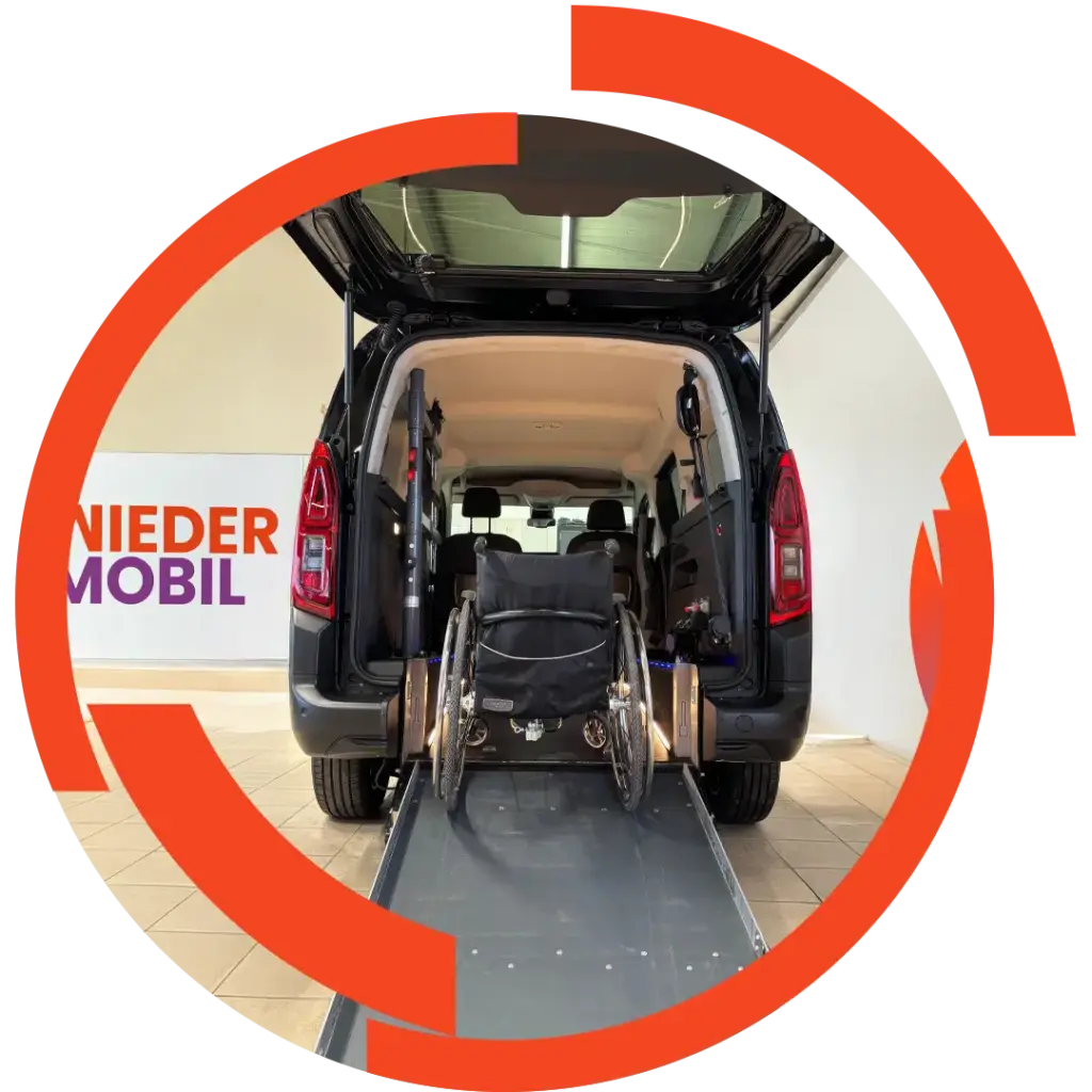 Rollstuhlgerechter dunkler Kleinbus mit geöffneter Heckklappe und ausgefahrener Rampe, Rollstuhl steht mittig auf der Rampe.