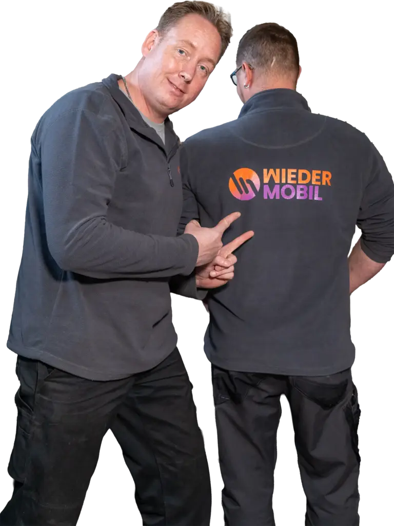 Zwei Männer in dunkelgrauen Pullovern, einer zeigt auf den Rücken des anderen mit farbigem Logo und Schriftzug "WIEDER MOBIL".