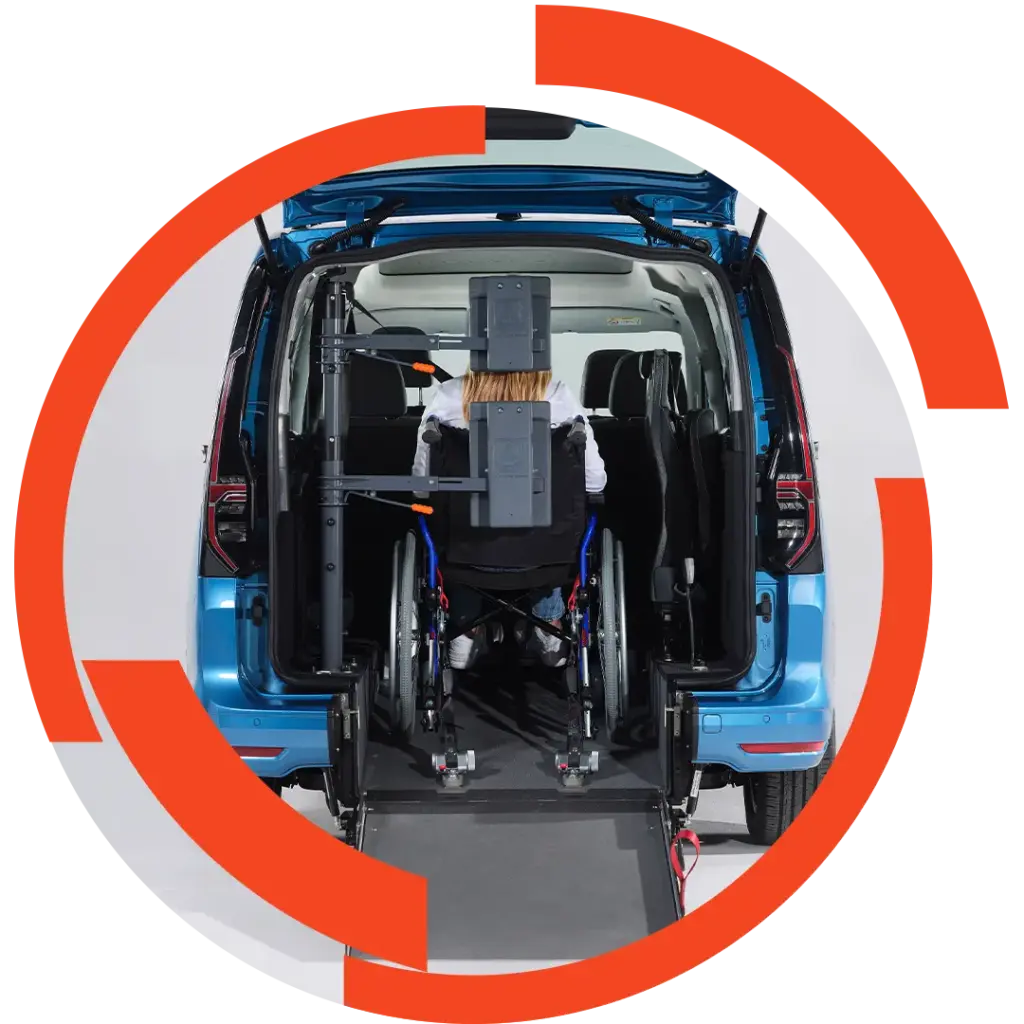 Rollstuhlfahrer wird per Heckrampe in ein blaues Fahrzeug geschoben; Hebe- und Haltevorrichtung seitlich montiert.