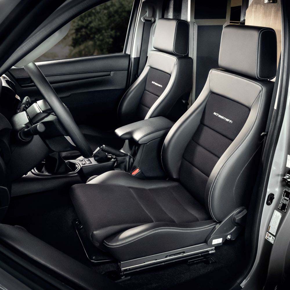 Vordersitze eines Autos in schwarzem Leder/Stoff mit konturierten Seitenwangen, Kopfstützen und heller Ziernaht, Fahrerarmlehne sichtbar.