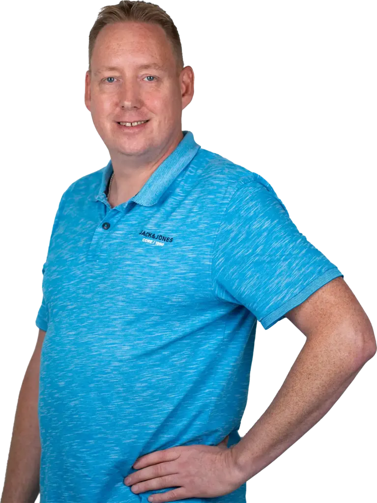 Mann lächelnd in blauem Polohemd mit Hand in der Hüfte, Nahporträt bis Oberschenkel, heller Hintergrund.