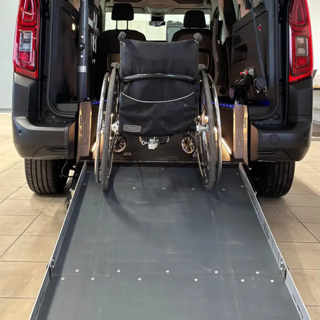 Rollstuhl auf einer ausklappbaren Rampe, verladen in den geräumigen Laderaum eines Fahrzeugs mit offenem Heck.