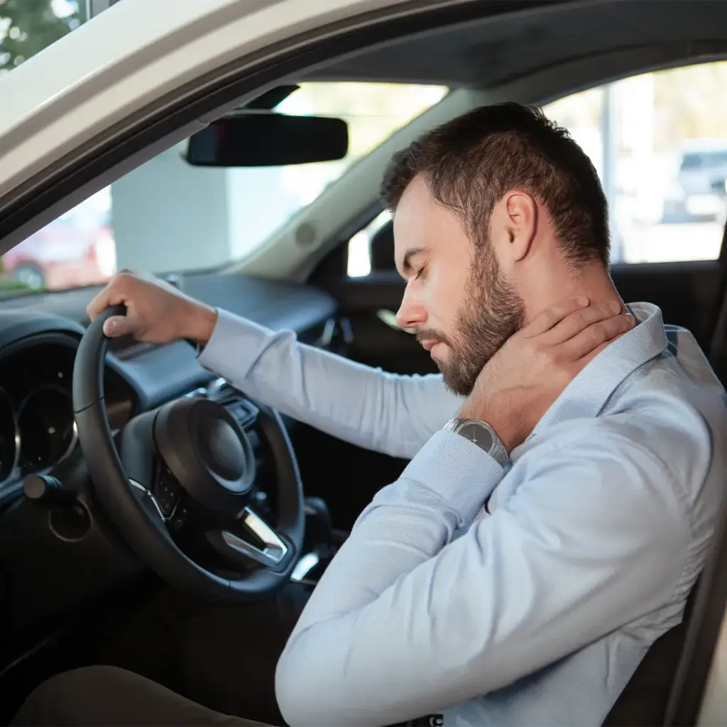 Mann im Auto fasst sich mit schmerzverzerrtem Gesicht den Nacken, offenbar Nacken- oder Schulterschmerzen.