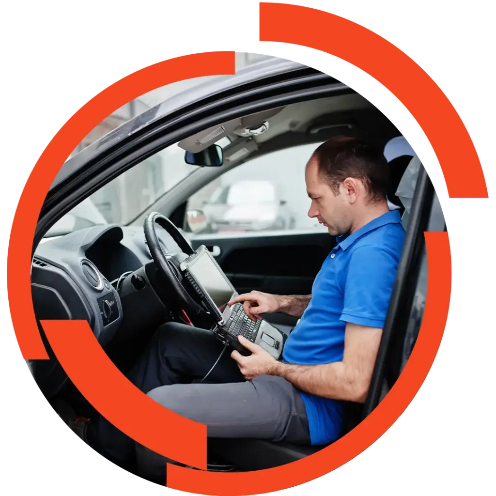 Mann in blauem Polo sitzt im Auto und bedient ein Diagnosegerät am Beifahrersitz, Blick auf Bildschirm und Tastatur