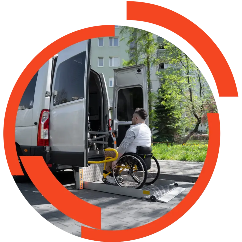 Mann im Rollstuhl fährt über Lift in einen Kleinbus, umgeben von städtischem Hintergrund mit Bäumen und Wohngebäude.
