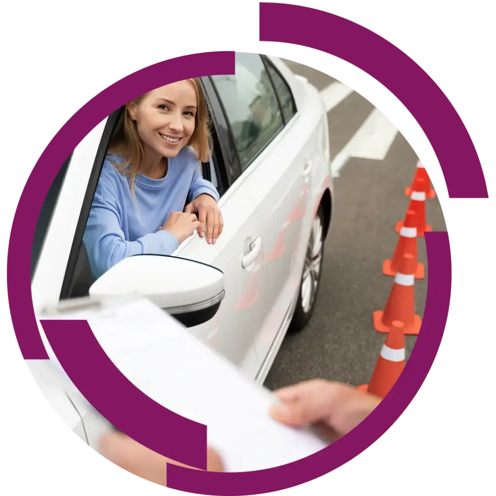 Frau lächelnd im offenen Fenster eines weißen Autos neben Verkehrshütchen, vermutlich bei einer Fahrprüfung.