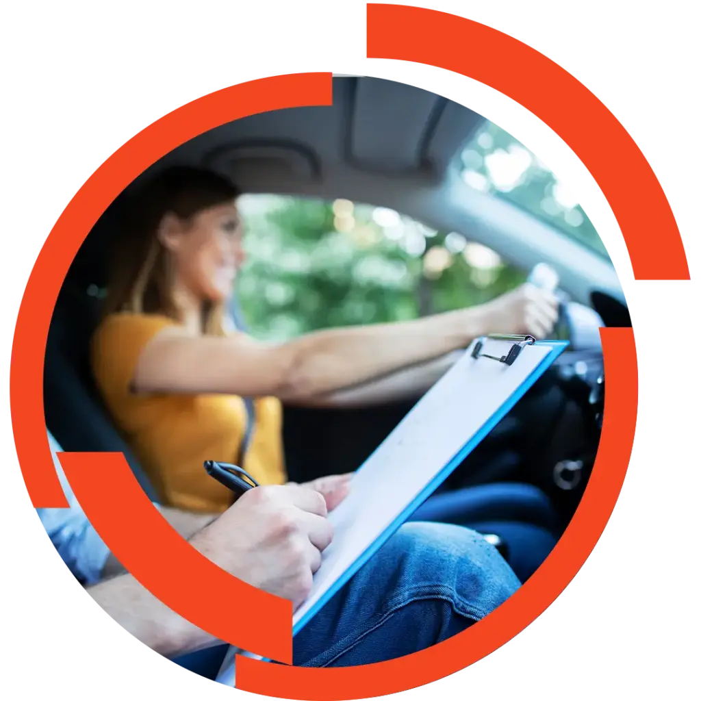 Fahrlehrerin sitzt am Steuer eines Autos, Fahrlehrer notiert auf Klemmbrett während er die Prüfung bewertet.