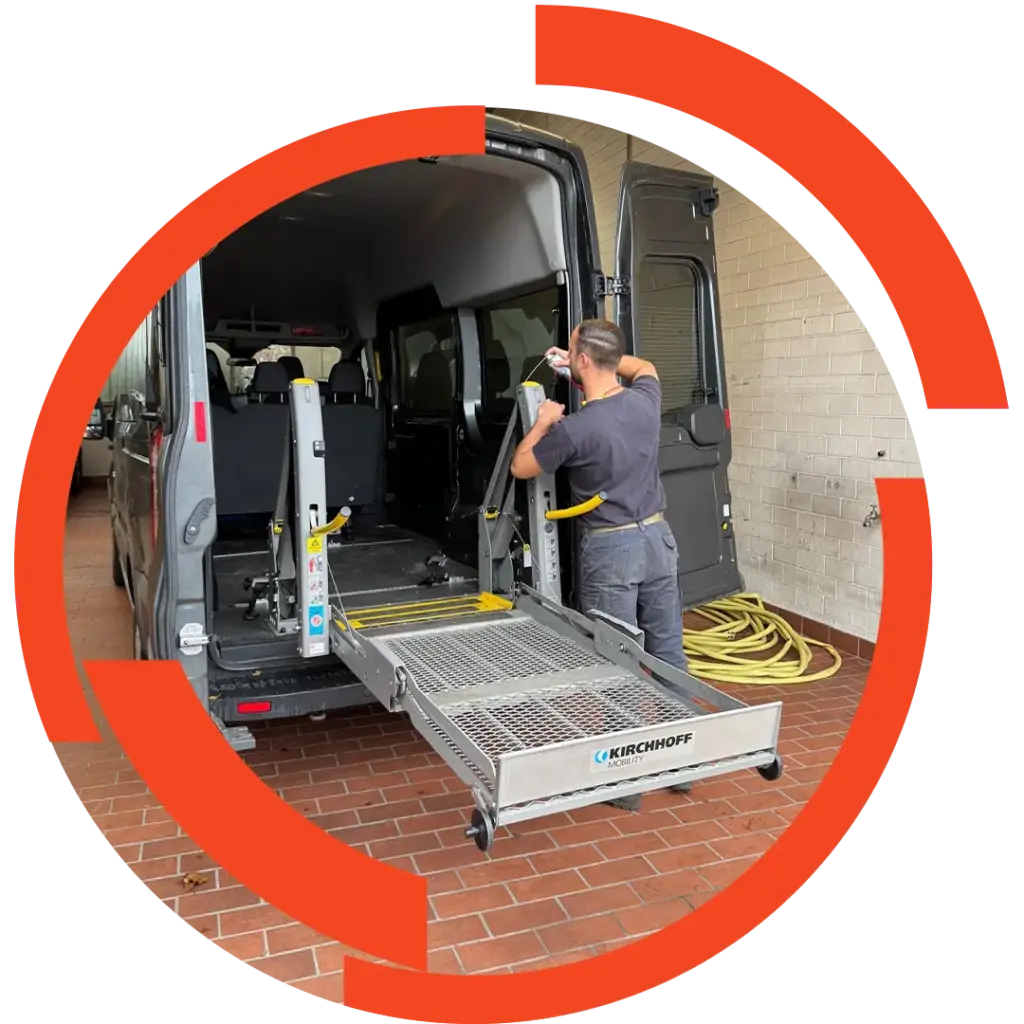 Mitarbeiter montiert oder wartet eine ausklappbare Rollstuhlrampe am Heck eines Transporters, markiertes Metallgitter mit KIRCHHOFF-Logo.