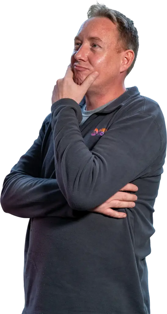 Mann in dunkelgrauem Pullover steht nachdenklich mit Hand am Kinn und Blick nach oben rechts.