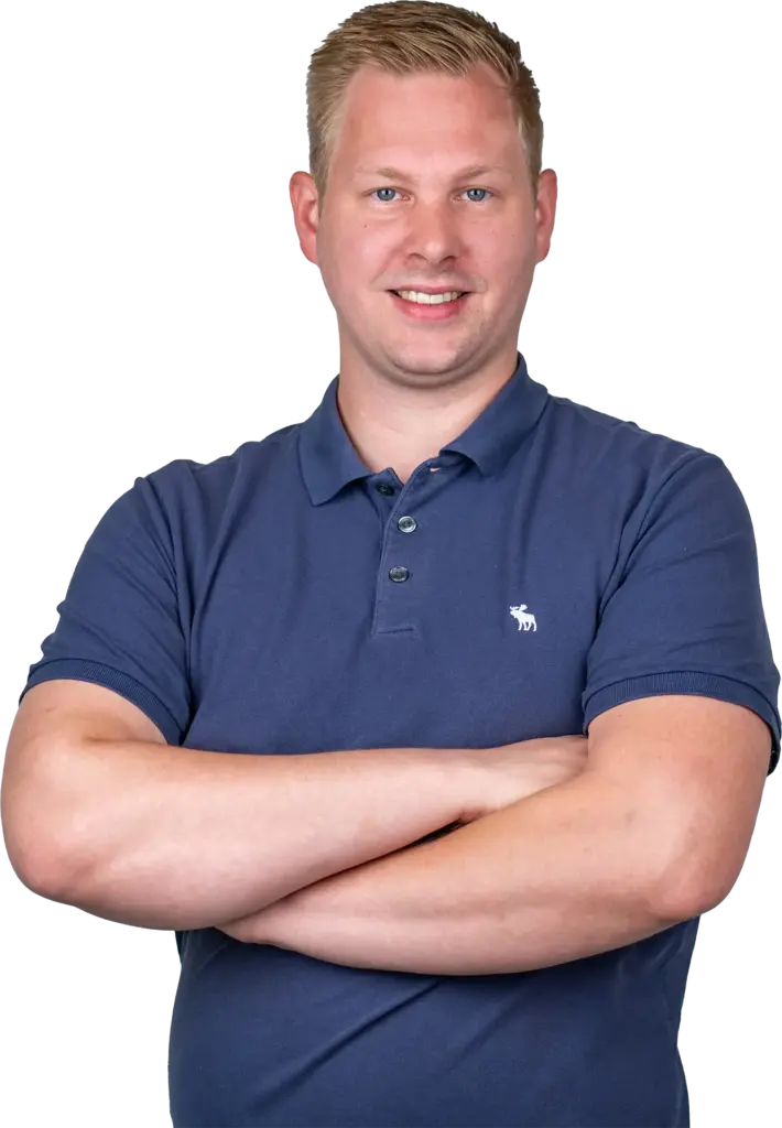 Junger Mann mit blonden Haaren und blauem Polohemd, lächelnd und mit verschränkten Armen vor hellem Hintergrund.