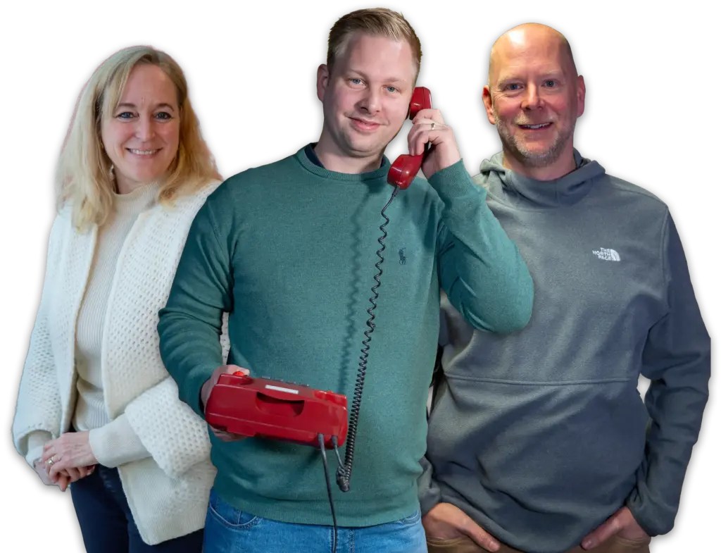 Drei lächelnde Erwachsene vor schwarzem Hintergrund; mittlerer Mann hält ein rotes Telefon, links Frau in weißem Strickpullover, rechts Mann in grauem Hoodie.