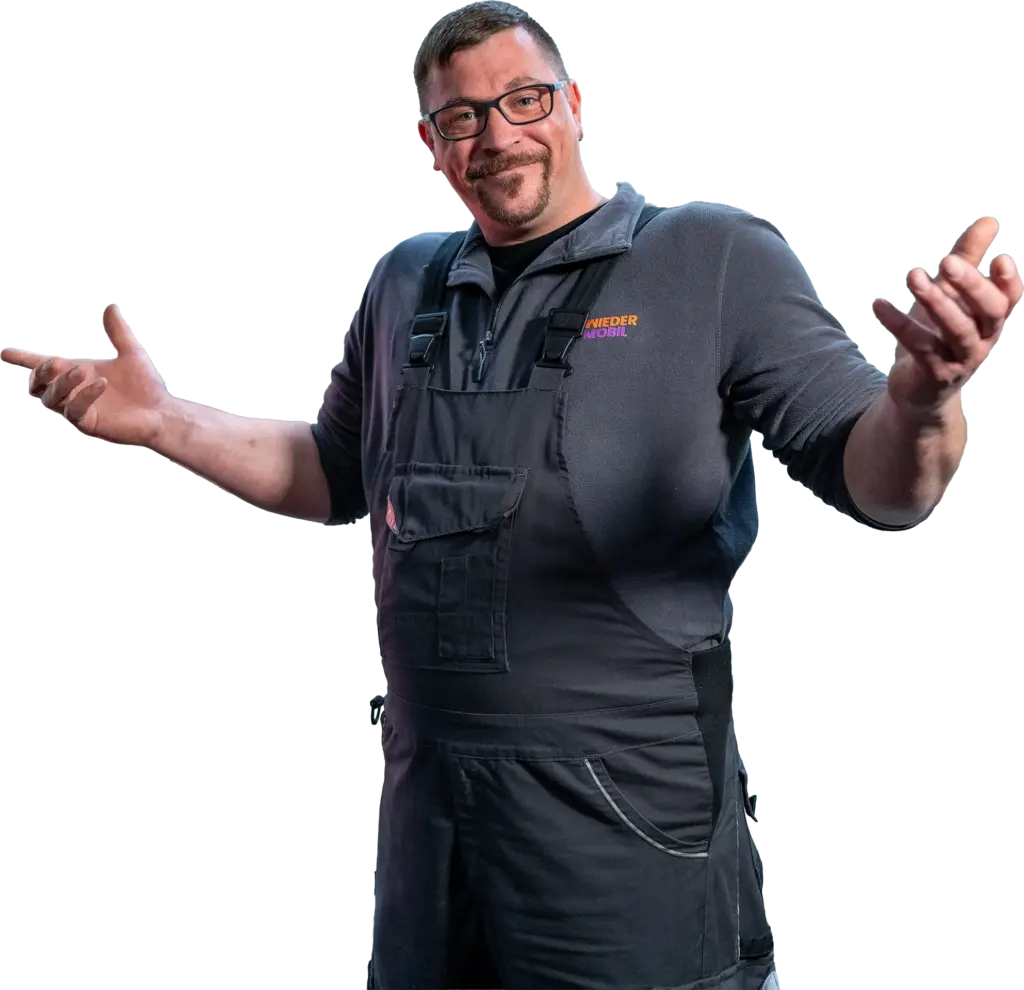 Mann mit Brille und Schnurrbart in dunklen Arbeitslatzhosen und Pullover, die Arme einladend ausgestreckt vor gestreiftem Hintergrund