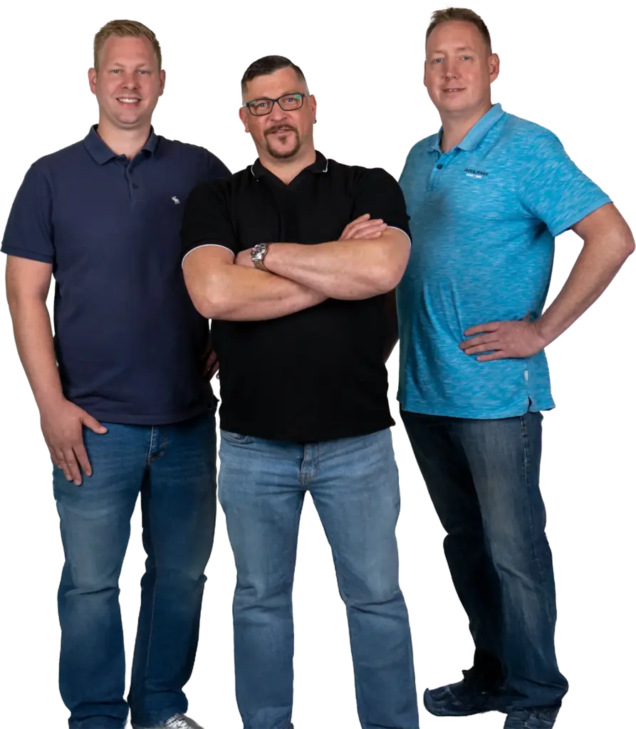 Drei lächelnde Männer in Polo-Shirts und Jeans, der mittlere mit verschränkten Armen und Brille.