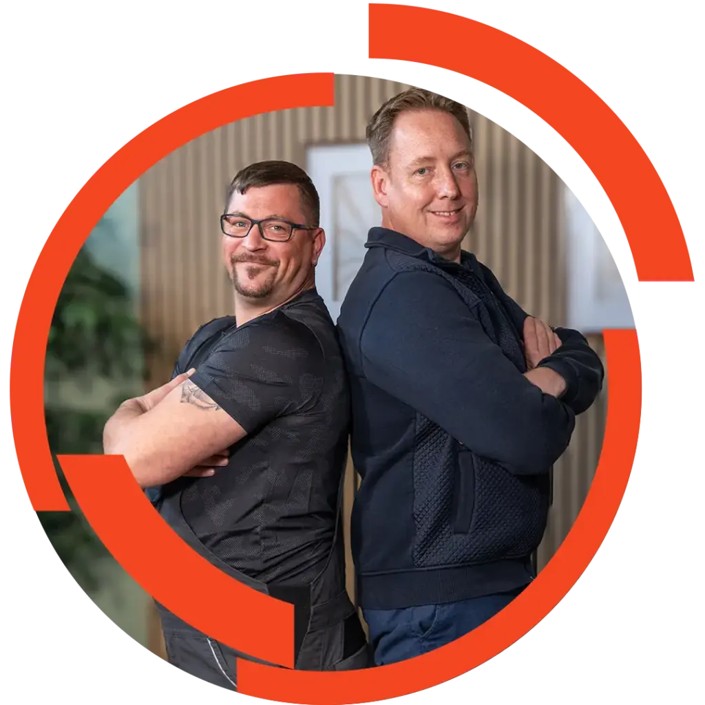 Zwei Männer stehen Rücken an Rücken mit verschränkten Armen und lächeln, roter Kreisrahmen um sie.
