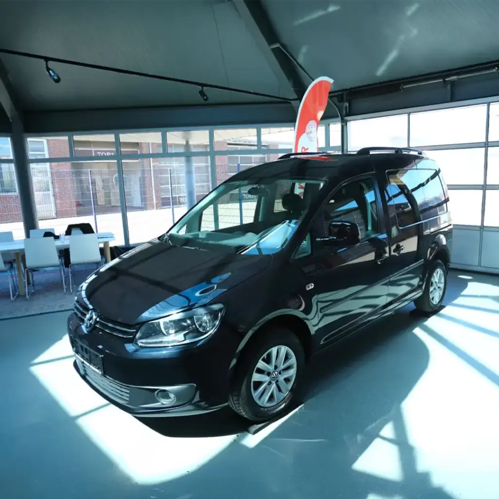 Schwarzer Volkswagen Caddy im Showroom, rollstuhlgerechte Großraumlimousine mit hoher Dachlinie und Schiebetür.