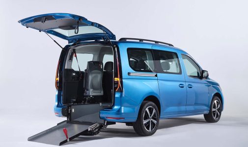 Blauer Kleinbus mit geöffneter Heckklappe und ausgeklappter Rollstuhlrampe, Blick in den Innenraum mit sichtbaren Sitzen vor neutralem hellgrauem Hintergrund.